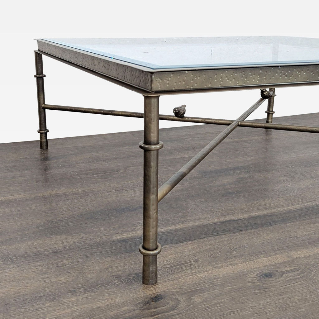 Coffee table with beveled glass top, hammered bronze apron, and iron stretchers holding three bird figures.