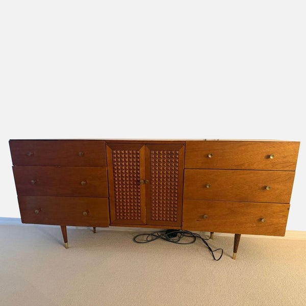 Mid-century modern dresser with six drawers, center cabinet, and brass-accented legs in a warm wood finish.