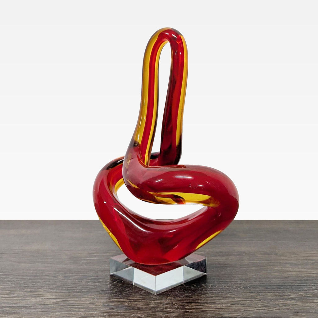 Modern art glass accent with intertwined red and amber tones, supported by a sturdy clear base.