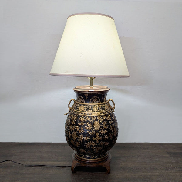 Elegant table lamp with black base, gold floral accents, and a cream shade for warm, stylish lighting.
