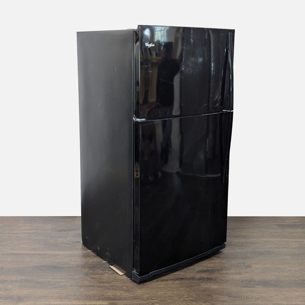 Whirlpool refrigerator in classic black, featuring a top freezer and ample storage, with minor exterior wear.
