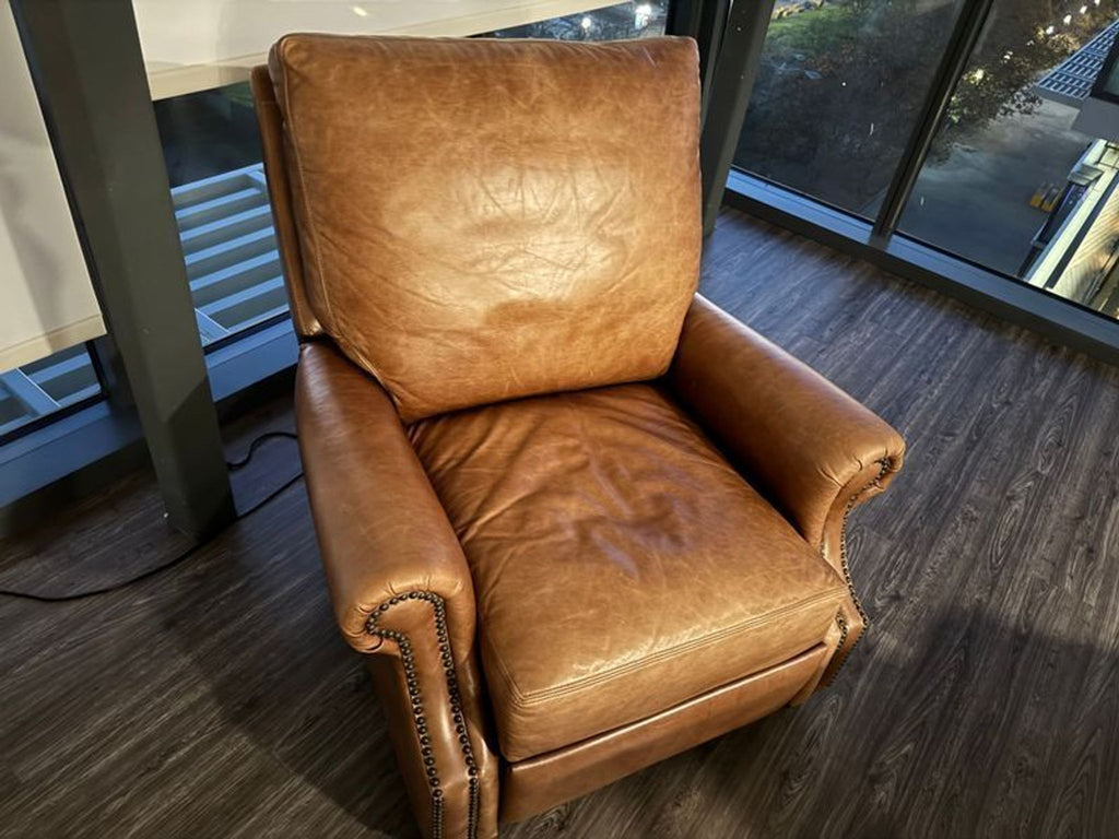 1. Brown leather Pottery Barn lounge chair with rolled arms and nailhead trim, set on dark wood flooring.  