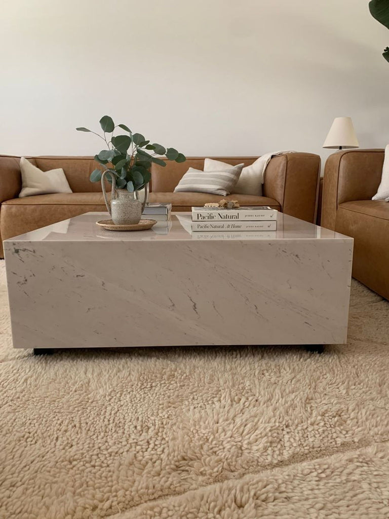 2. Rove Concepts marble coffee table in a cozy living room, styled with books and a plant, between tan sofas.