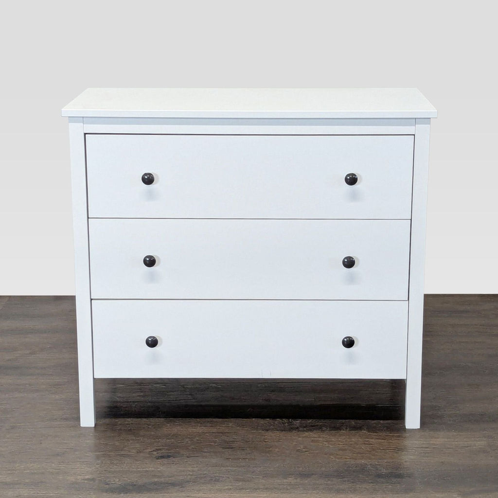White modern dresser with three drawers and black knobs, ideal for bedroom storage.