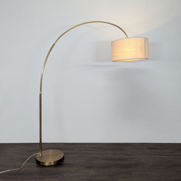 Modern brass arc floor lamp with a neutral fabric drum shade and round base, ideal for living spaces.