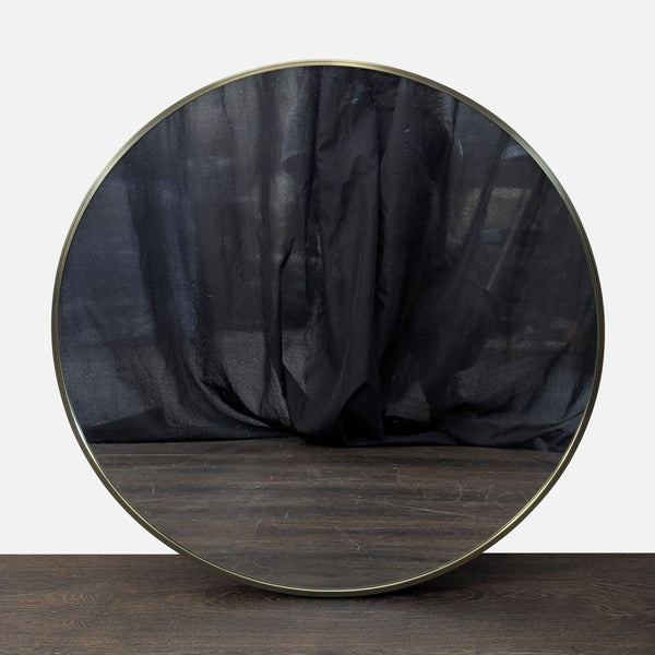 1. Round mirror with a thin metallic frame, reflecting a dark curtain and placed on a wooden surface.