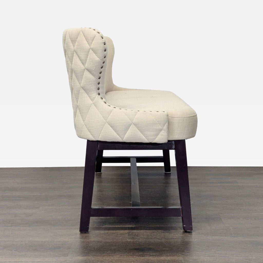 Elegant bench featuring a winged, quilted back, nailhead detail, and sturdy wood base for support.