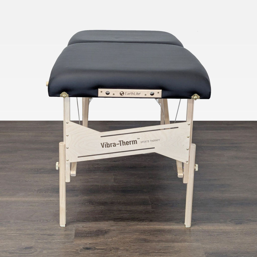 Black padded Earthlite massage table featuring wooden frame, shown set up and ready for sports therapy or relaxation.