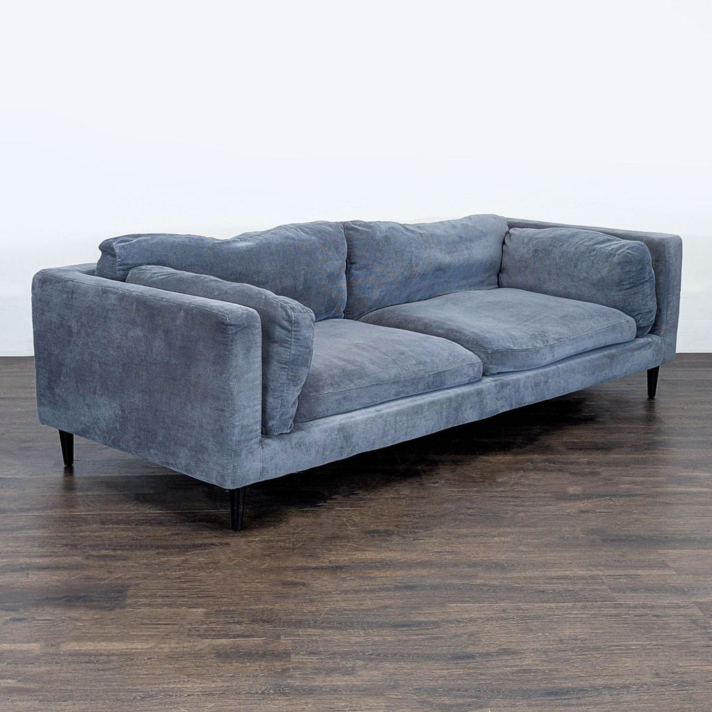 2. Angled view of a plush blue Moe's Home Collection 3-seat sofa with wide arms and soft fabric upholstery.