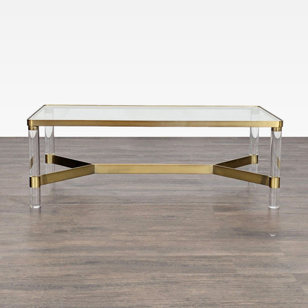 Hollywood Regency-style coffee table with glass top, brass accents, and round Lucite legs, inspired by Karl Springer.