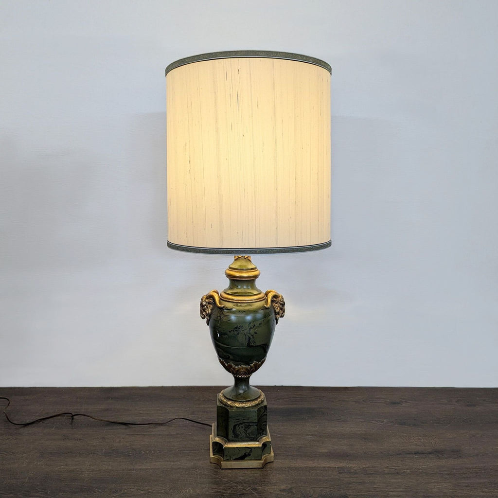 Neoclassical table lamp with green urn base, gold ram handles, and cream drum shade, evoking classical elegance.