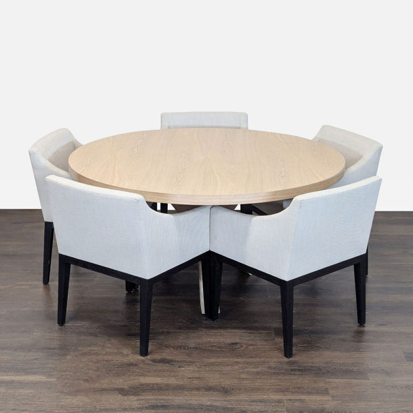 Round light wood dining table with cross-base and four cream upholstered chairs, elegant farmhouse style.