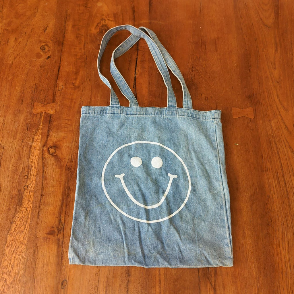 Madewell denim purse with a big white smiley face, double straps, and open top design.