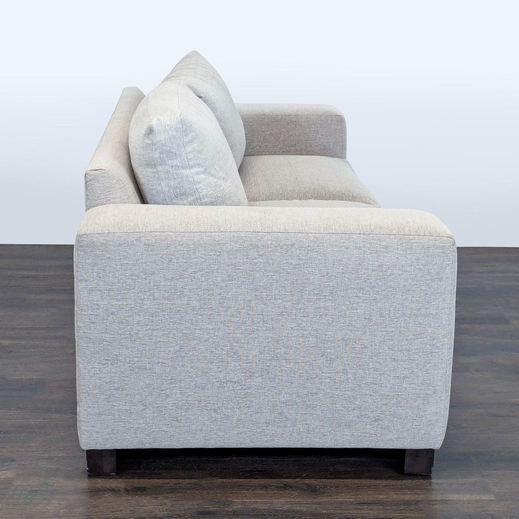 3. Side profile of a Kreiss Loveseat in light gray fabric, featuring wide arm and sturdy wood base.