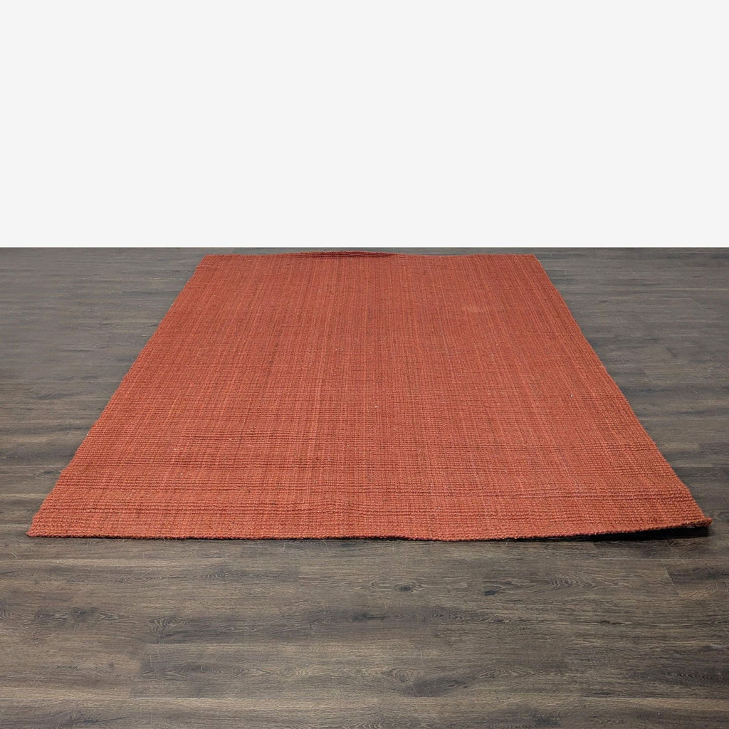 1. Handwoven jute rug in rich rust color from West Elm, shown on a dark wood floor, measuring 5x8 feet.  