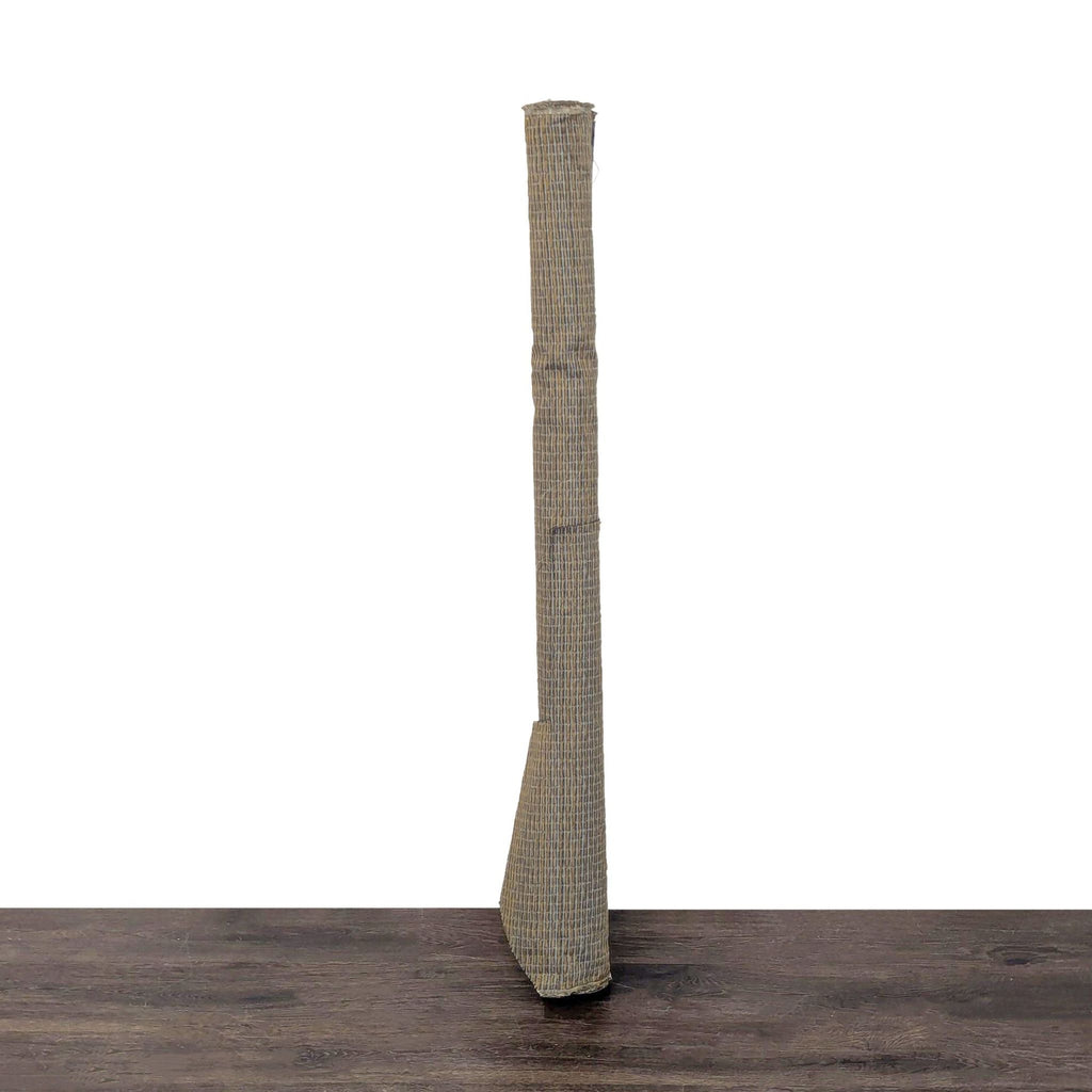 Tall, textured object with a woven blue and tan fabric, standing upright on a dark wooden surface.  