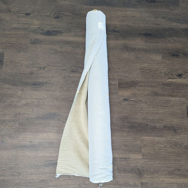 Roll of textured neutral fabric, suitable for upholstery, resting on a plain surface.  