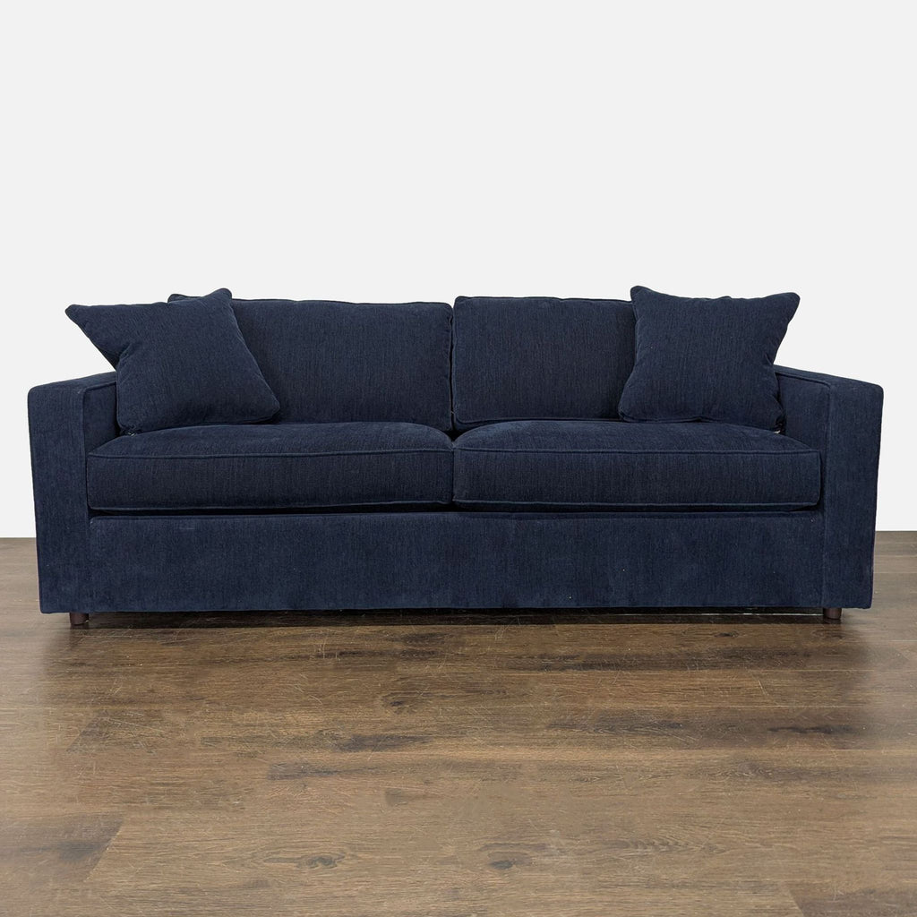 Navy blue sleeper sofa with two pillows, seats three, and converts into a pull-out bed for guests.