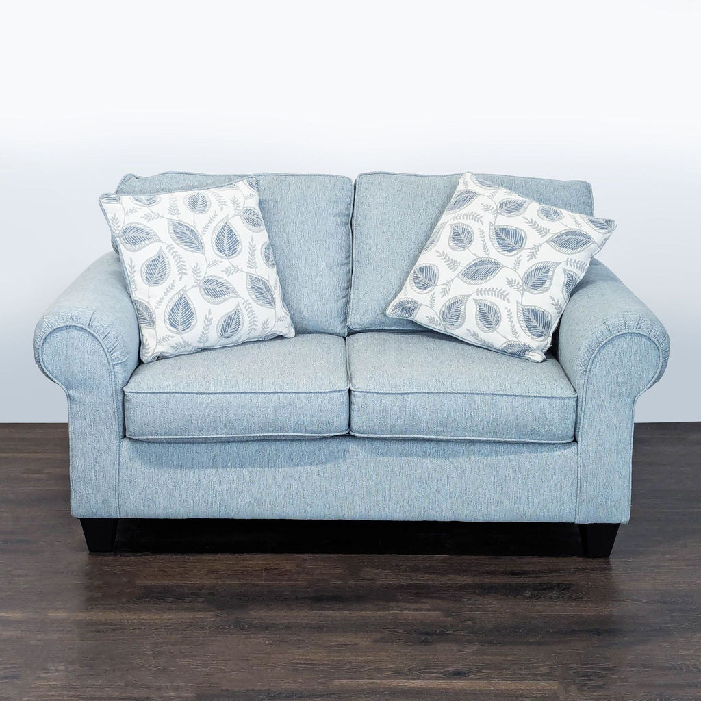 Light blue Minhaus loveseat with leaf accent pillows, rolled arms, and dark wooden legs in a modern style.