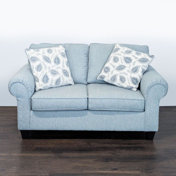 Light blue Minhaus loveseat with leaf accent pillows, rolled arms, and dark wooden legs in a modern style.