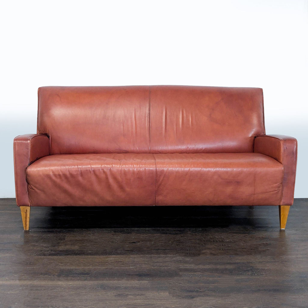 Brown leather mid-century modern loveseat with angled wood legs, compact and stylish for two-person seating.