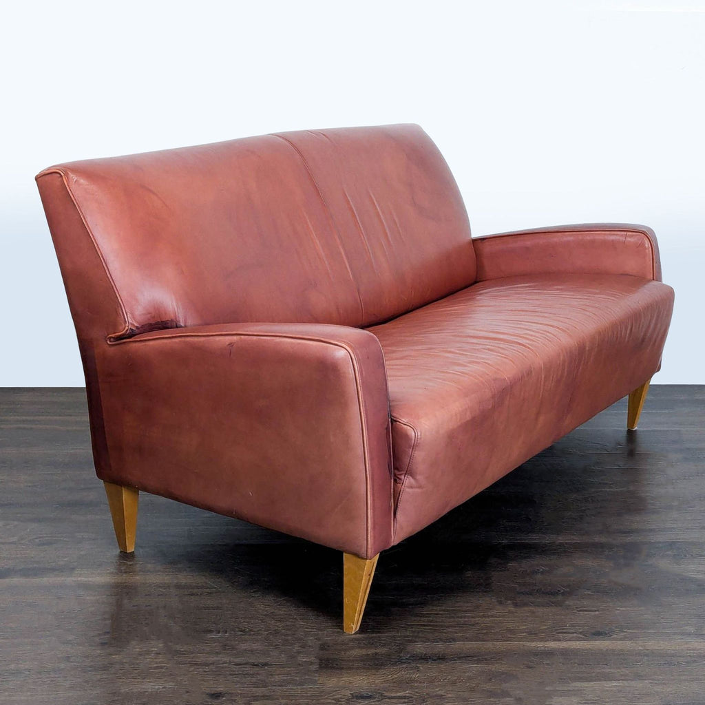 Mid-century modern loveseat in brown leather, featuring smooth upholstery and slanted wooden legs, seats two.
