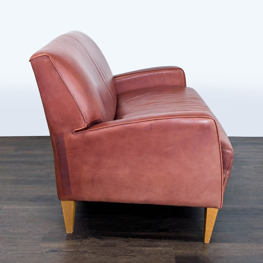 Compact brown leather loveseat with angled wooden legs, contemporary design for living rooms or offices.