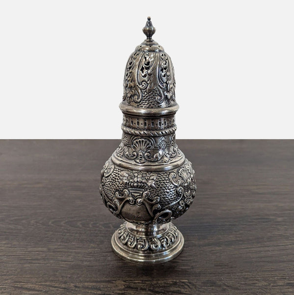 Ornate antique silver sugar caster with floral motifs, pierced dome lid, finial, pedestal base, and engraved "1907".