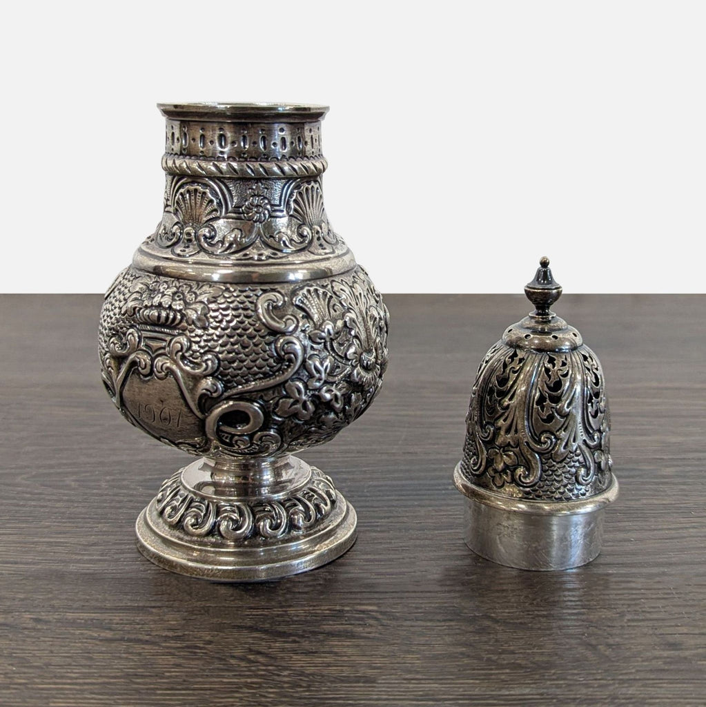 Highly decorative baluster-form muffineer with raised shell and scroll designs, removable dome lid, and visible aged patina.