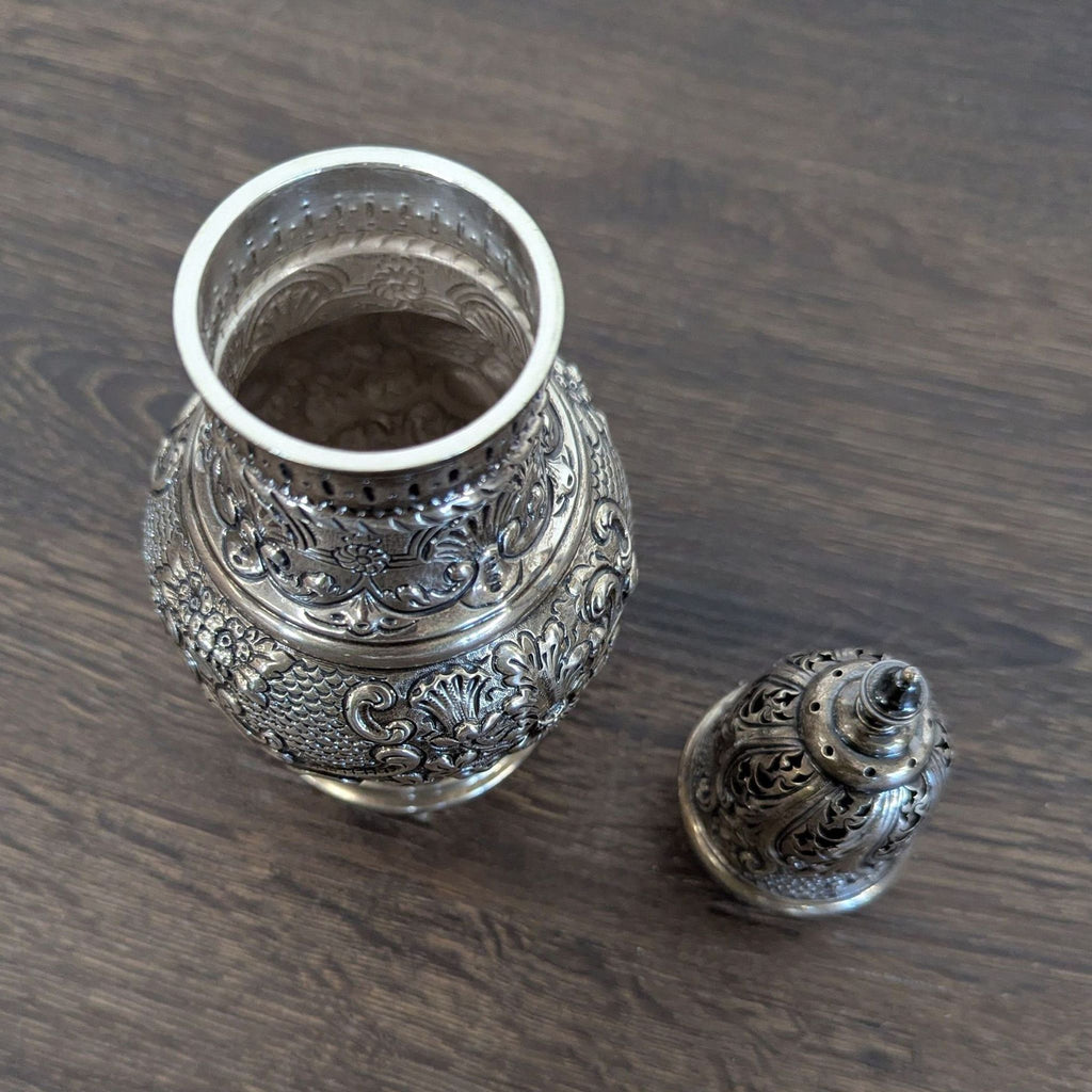 Antique silver sugar caster featuring intricate engraving, floral decorations, pedestal foot, and signs of tarnish and wear.
