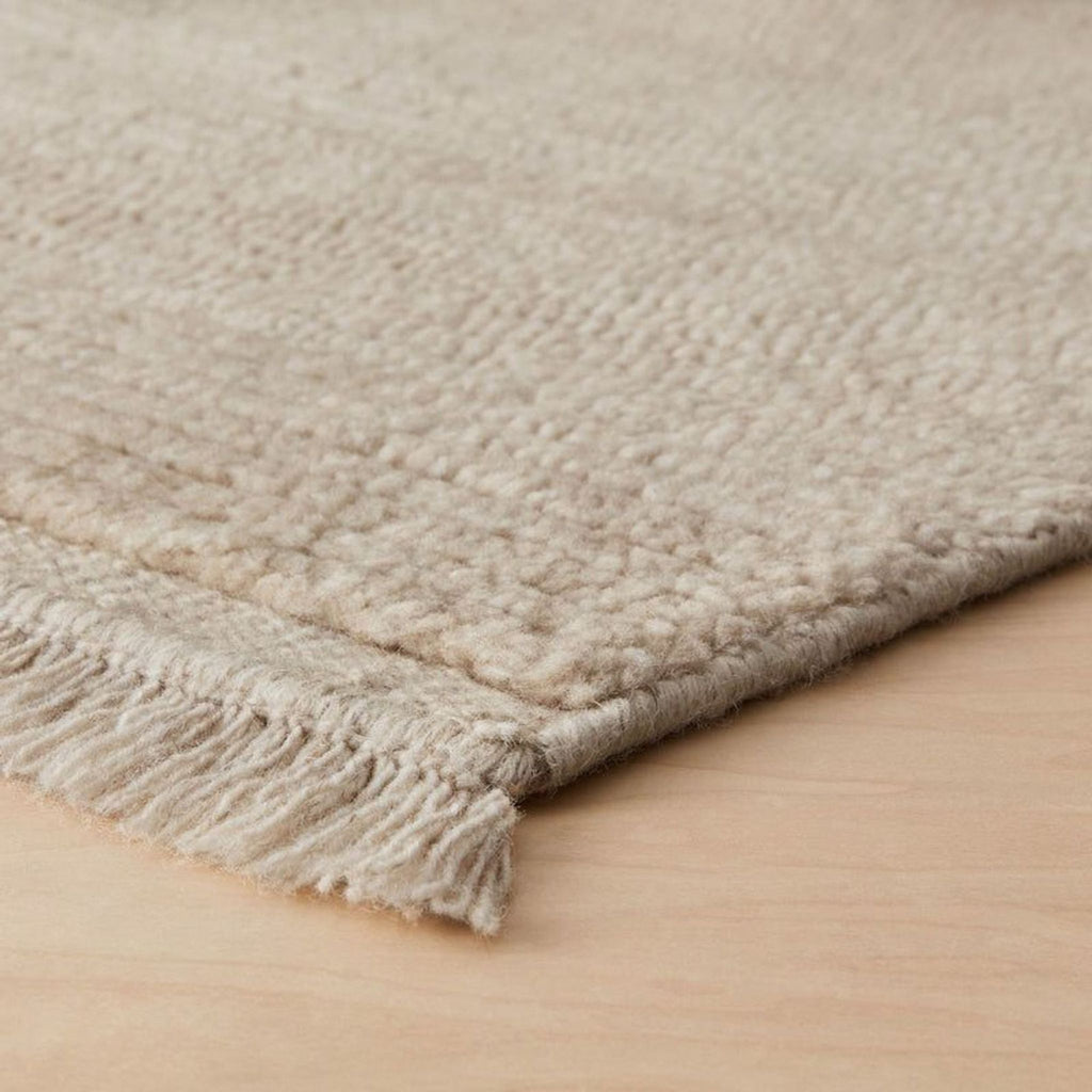 Neutral-toned Citizenry rug with a soft handwoven design, durable wool material, and decorative fringe detail.