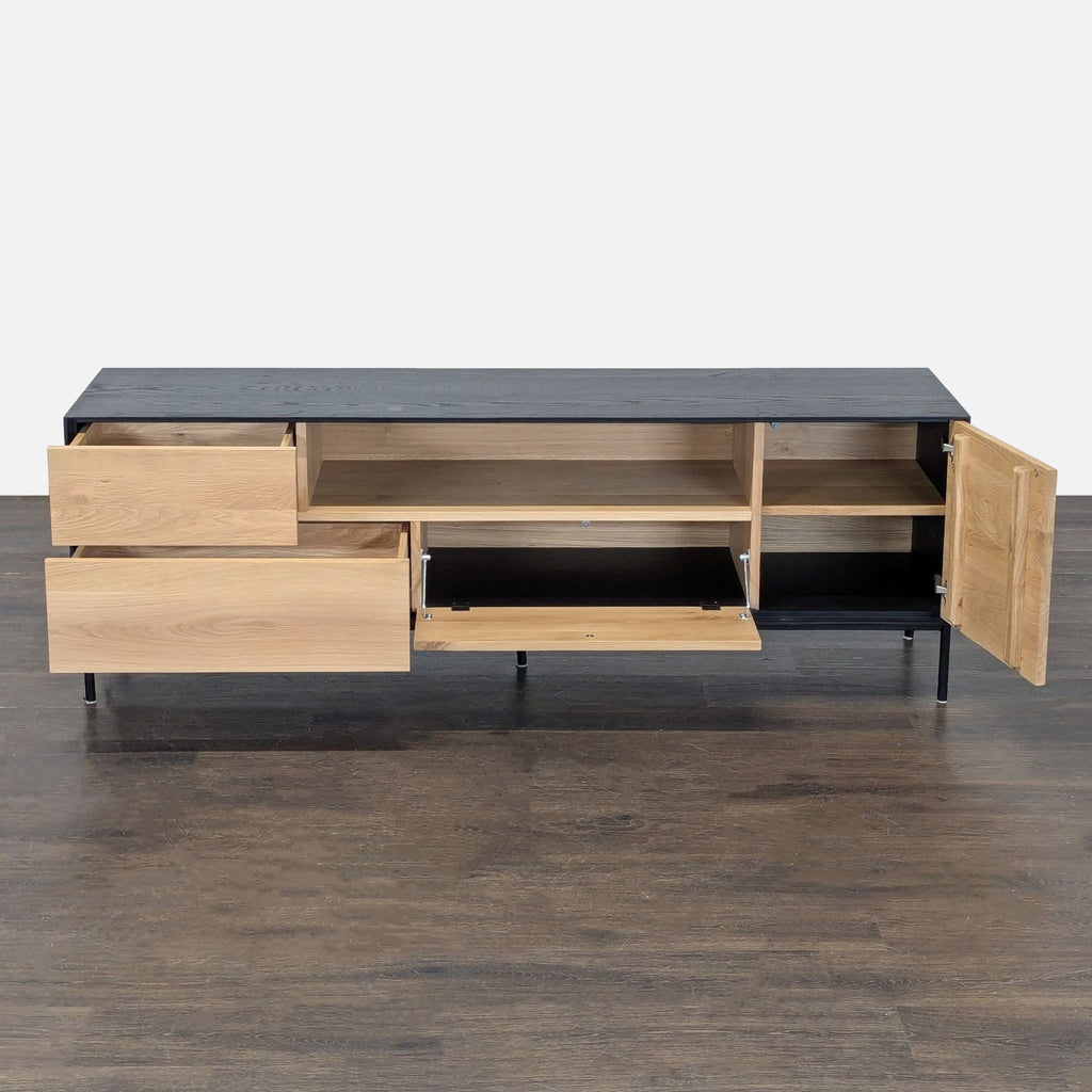 Modern entertainment center featuring natural wood front, black top, open shelf, drawers, and metal feet.