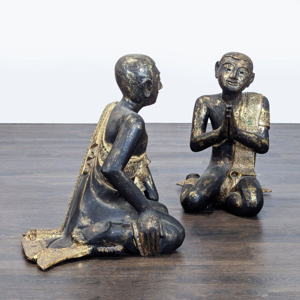 1. Two ornate sculptures of kneeling monks in conversation, with gold-embellished robes, on a wooden surface.  