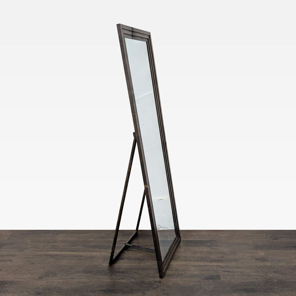 2. Side view of a freestanding mirror with a dark wooden frame and built-in support stand on a wood floor.