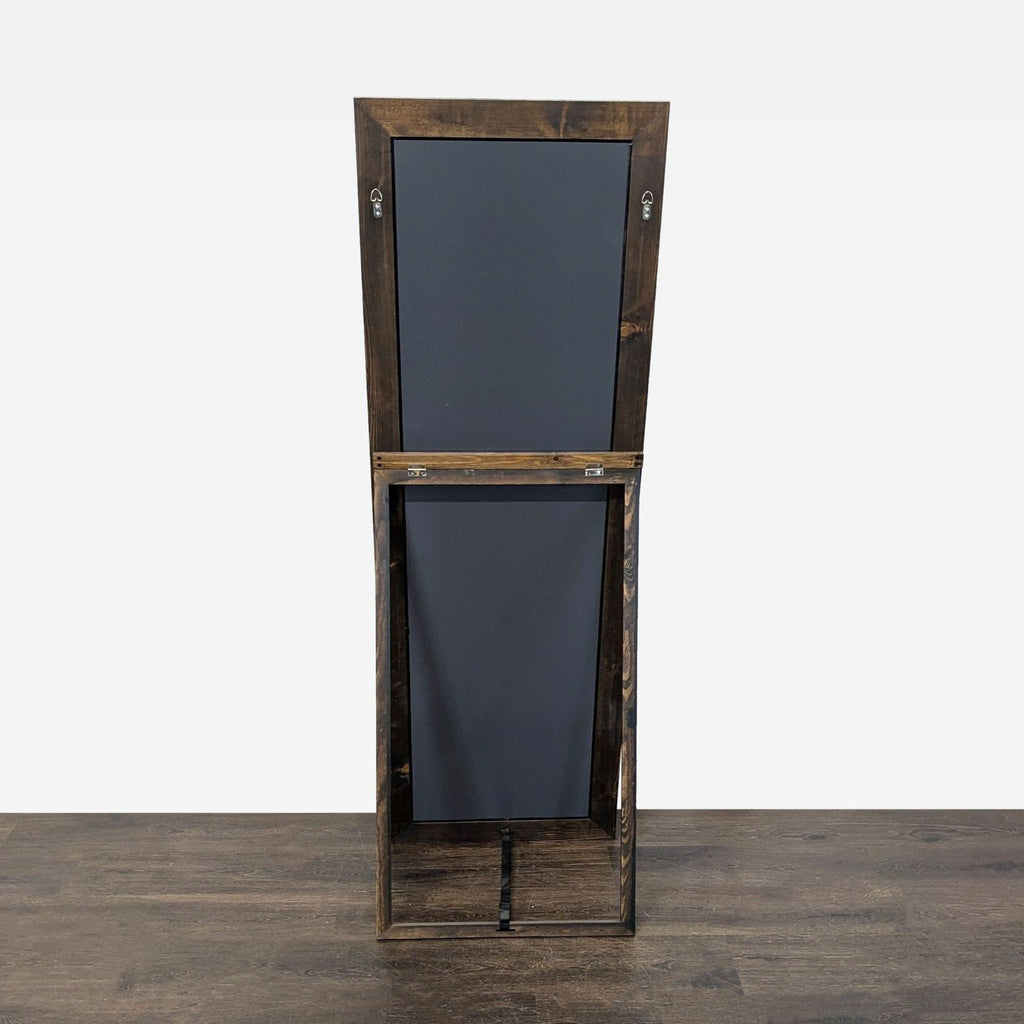 3. Rear view of rectangular mirror in a wooden frame, showing back panels and support stand, standing upright.