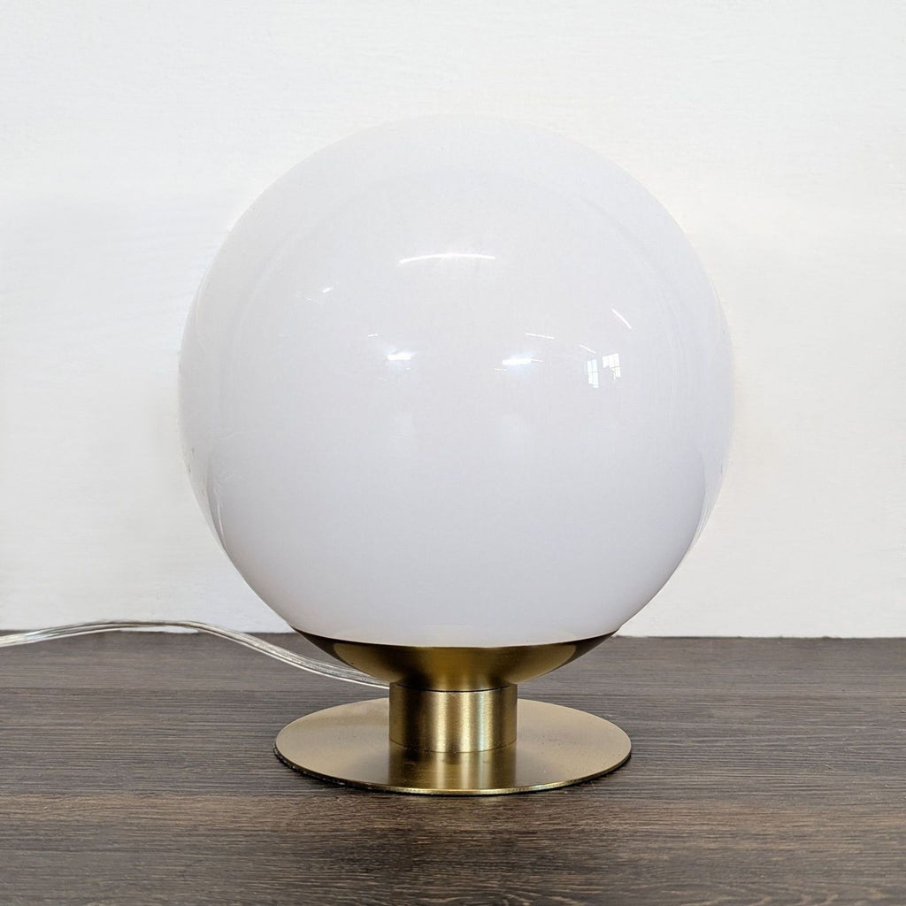 West Elm brass table lamp with a round white glass globe, casting warm light, modern and elegant.