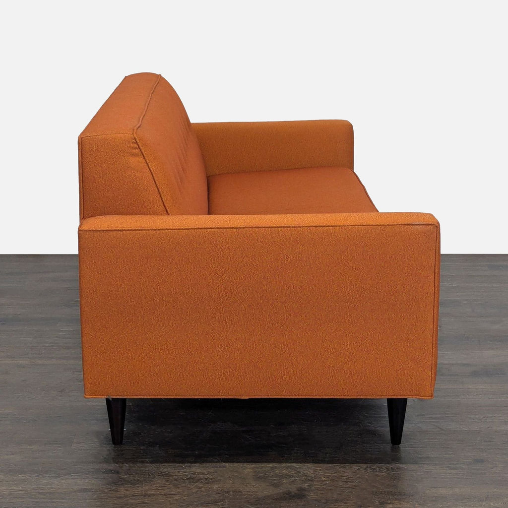 Modern 3-seater sofa in bright orange by Design Within Reach, with sleek design and sturdy dark legs.
