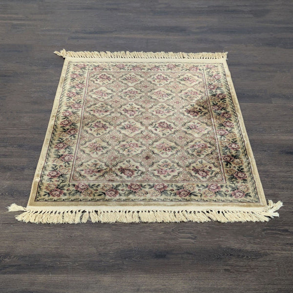 Vintage-style area rug with beige, pink, and green floral patterns, bordered design, and decorative fringe ends.