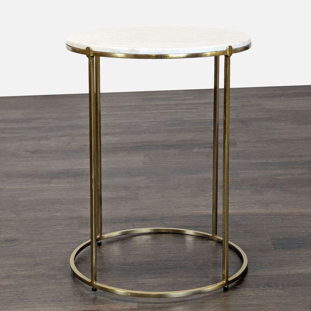 A round end table featuring a white marble top and slim gold metal frame, placed on a wooden floor.