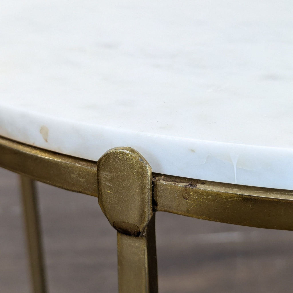 Close-up of a round end table with a white marble top and gold metal legs, highlighting the textured details.  