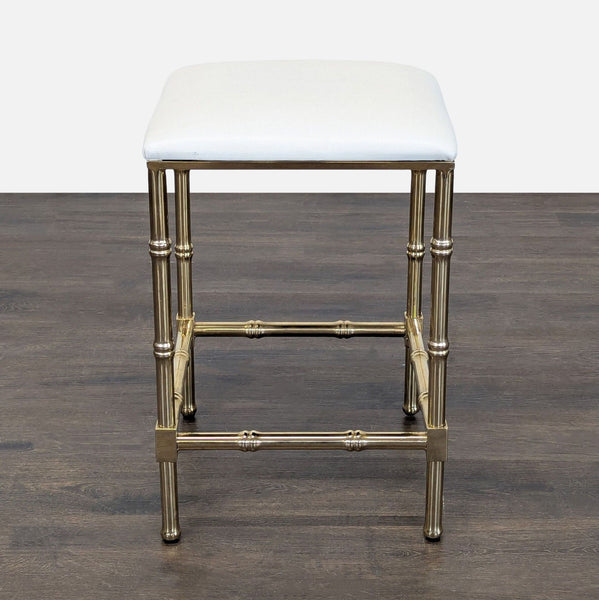 1. Brass-framed stool with a white textured cushion, shown on a dark wood floor, front view.
