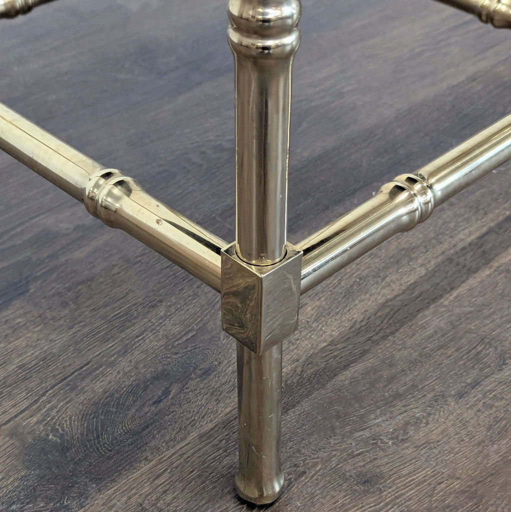 3. Detailed view of the brass leg joint and crossbars of a stool on wood flooring.