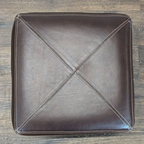 1. Top view of a square, dark brown leather ottoman with visible stitched seams and X pattern.