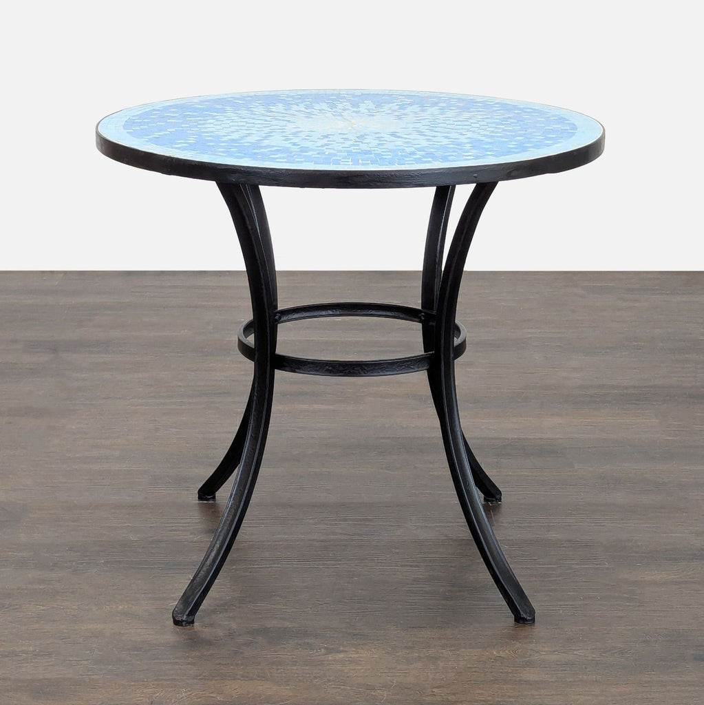 3. Side view of a Crate & Barrel round mosaic table with a blue tile top and curved black metal legs.