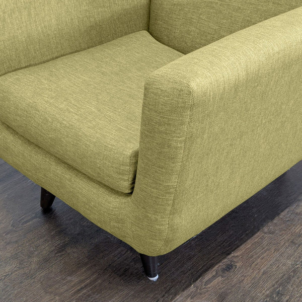1. Close-up of Joybird lounge chair in green fabric, showing armrest, seat cushion, and wood floor.