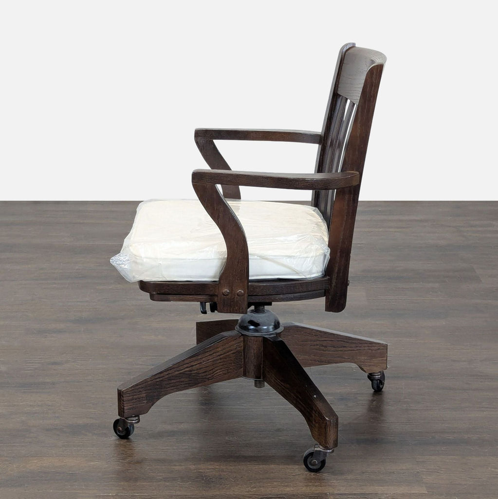 2. Side view of a Pottery Barn desk chair featuring curved wooden arms and a padded seat cushion.