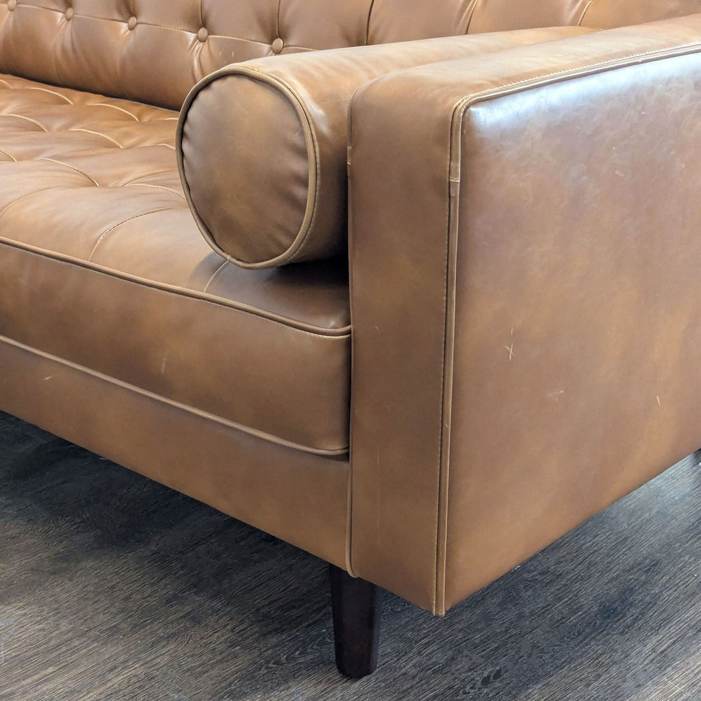 2. Close-up of the armrest and round bolster pillow of a brown leather HD Buttercup 3-seat sofa.