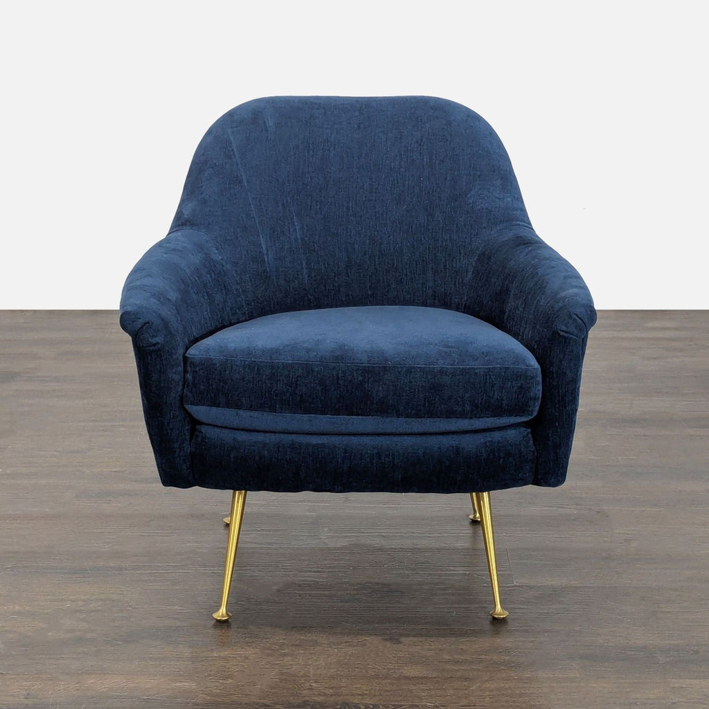 3. Front view of a West Elm lounge chair in deep blue fabric with curved arms and gold legs on a wood floor.