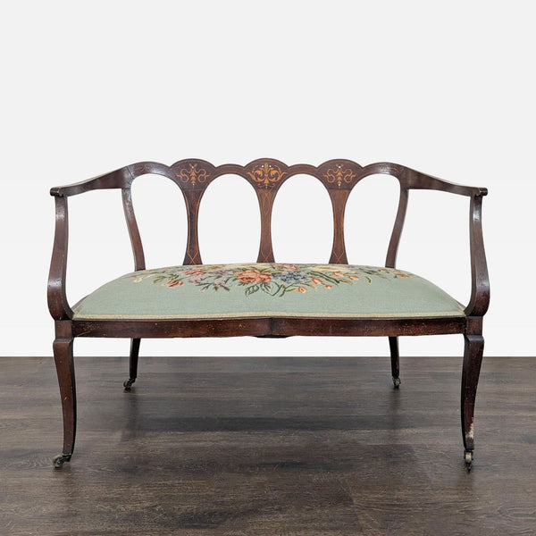Vintage loveseat with carved wood frame, triple-back design, and green floral embroidered seat cushion.