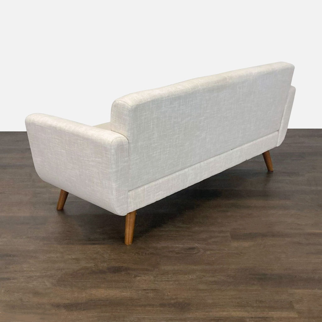 1. Back view of a modern light beige loveseat with wooden legs on a dark wood floor.
